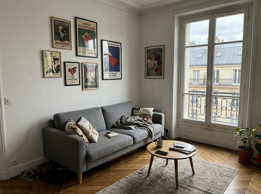 Salon lumineux avec une composition de cinq affiches de tailles différentes accrochées au-dessus d’un canapé